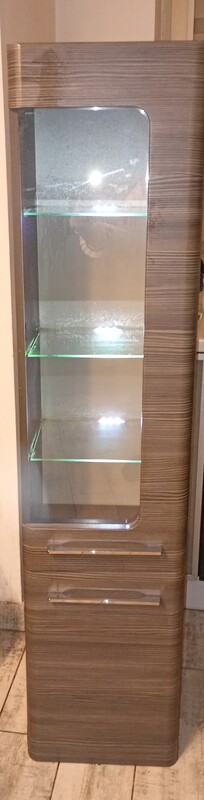 Elbląg Szafka łazienkowa, słupek podświetlana w stanie używanym. Posiada przeszklone drzwi i kilka półek wewnątrz.