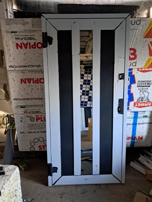 Elbląg Nowe, jeszcze nie montowane drzwi wejściowe aluminiowe, ciepłe. Otwierane na zewnątrz, lewe. Wymiary 100 cm x