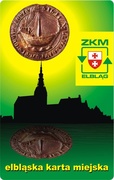 Projekt nr 1
Historyczna pieczęć elbląska z kogą „świeci” nad zarysem starówki. Odbicie pieczęci w wodzie symbolizuje kanał elbląski. Kolorystyka projektu nawiązuje do logo ZKM w Elblągu.